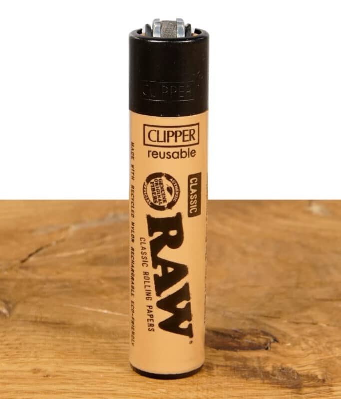 Clipper Feuerzeug im RAW Design, beige, auf einem Holztisch.