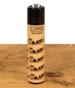Clipper Feuerzeug im klassischen RAW Logo Design, beige, auf einem Holztisch.