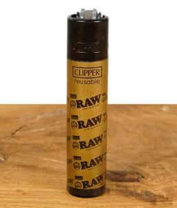 Clipper Feuerzeug mit RAW Logo in Gold auf einem Holztisch.