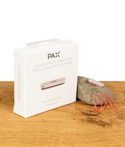 PAX Concentrate Insert Lid und O-Ring Ersatzteile in der Originalverpackung auf einem Holztisch, mit losen O-Ringen im Vordergrund.
