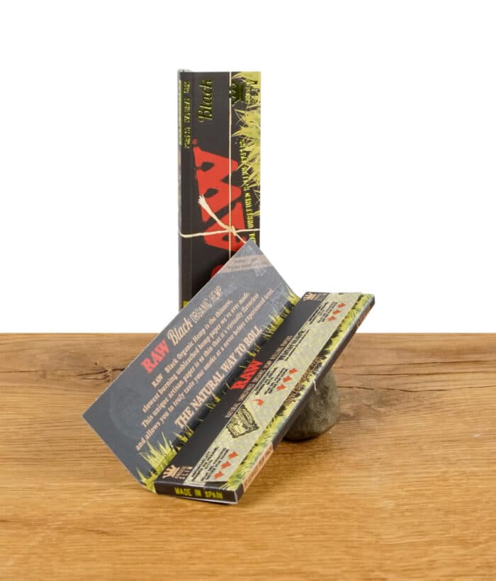 Geöffnete Packung RAW Black Organic Hemp Rolling Papers im King Size Slim Format, auf einem Stein präsentiert